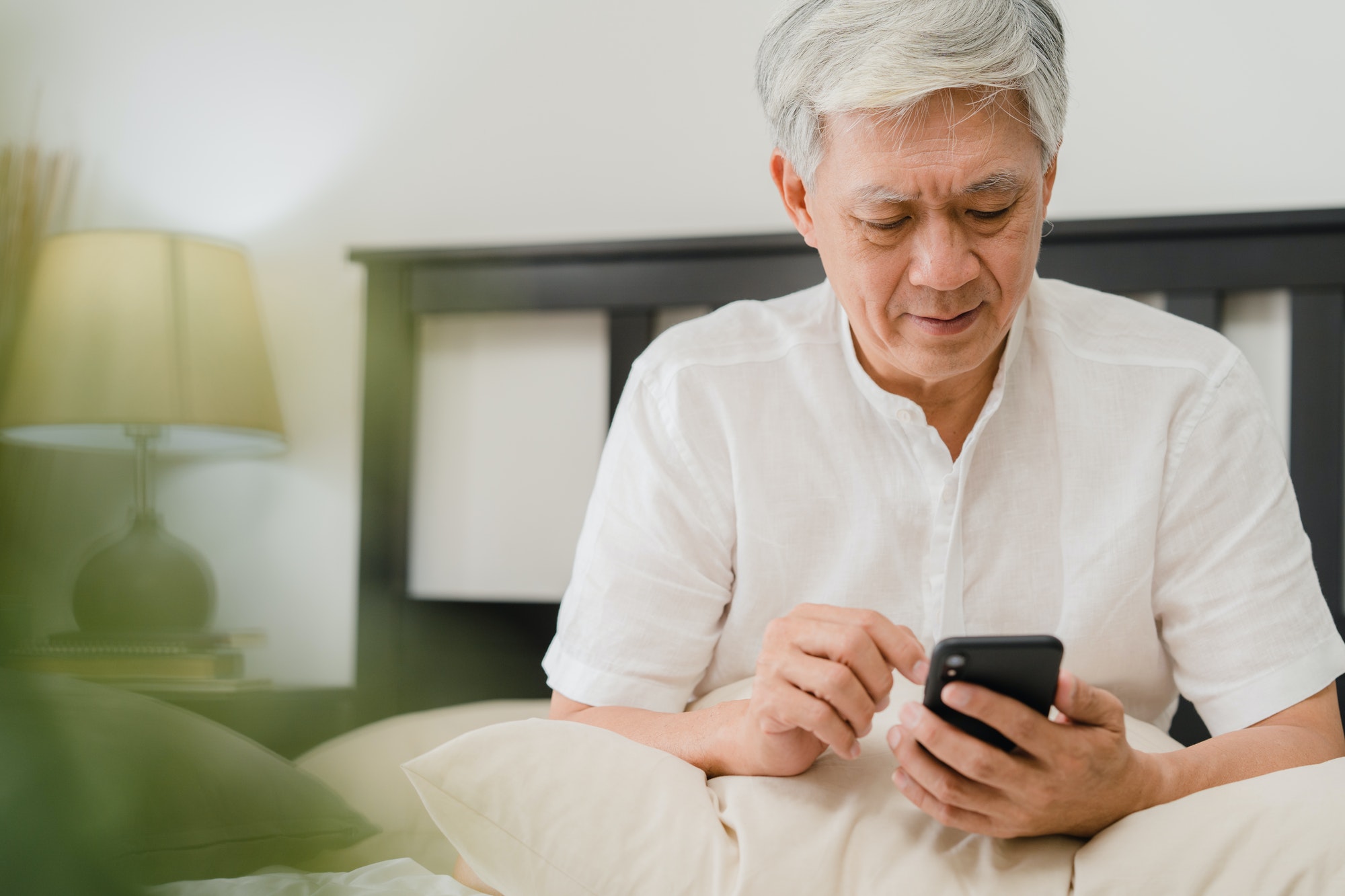 Asian senior men using mobile phone at home.